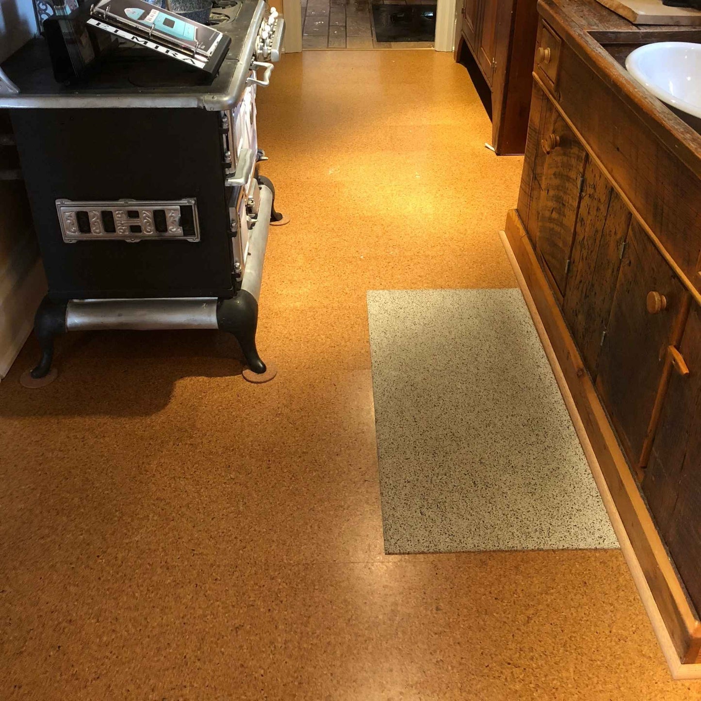 Pebble floating cork floor tiles in a kitchen, with a rubber cork mat in front of the sink and a vintage stove on furniture pads