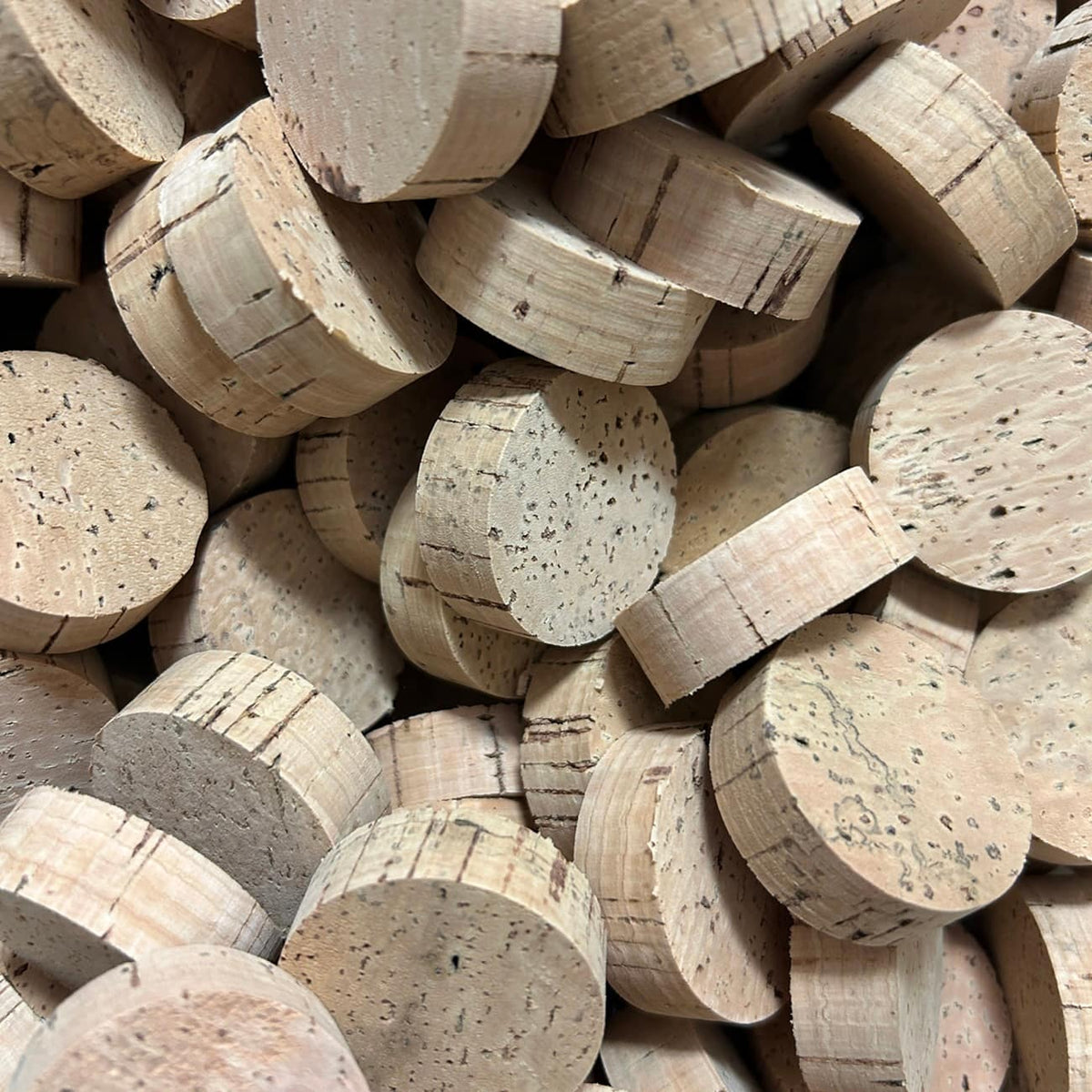 A pile of round cork rings in natural tan and beige tones, showing the textured cork surface and circular cross-sections.