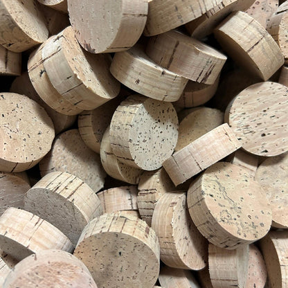 A pile of round cork rings in natural tan and beige tones, showing the textured cork surface and circular cross-sections.