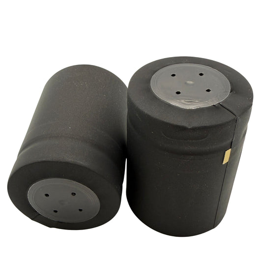 Two matte black closed cap PVC shrink caps with gold horizontal tear tab, close-up view to see the top and sides.