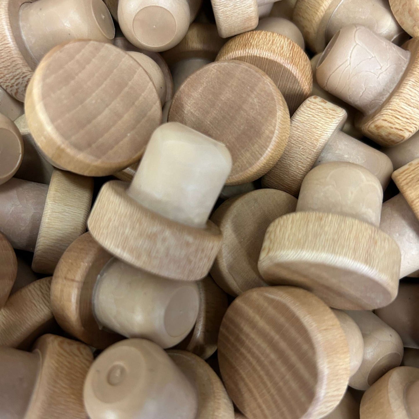 A pile of light natural wood round cork stoppers, showing visible wood grain tops with tan synthetic cork stems.