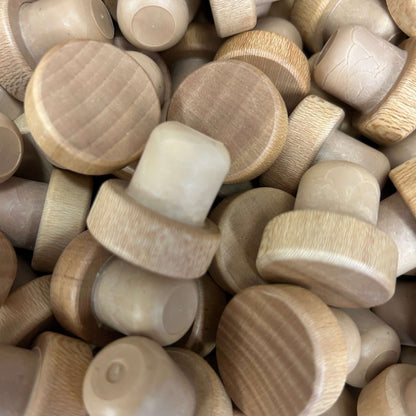 A pile of light natural wood round cork stoppers, showing visible wood grain tops with tan synthetic cork stems.
