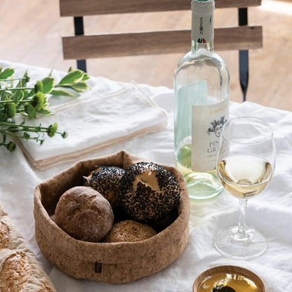 Folded cork fabric bowl on a dinner table holding bread.