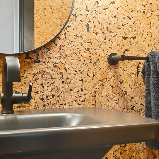 Bathroom sink with metallic faucet against a cobblestone black cork wall.